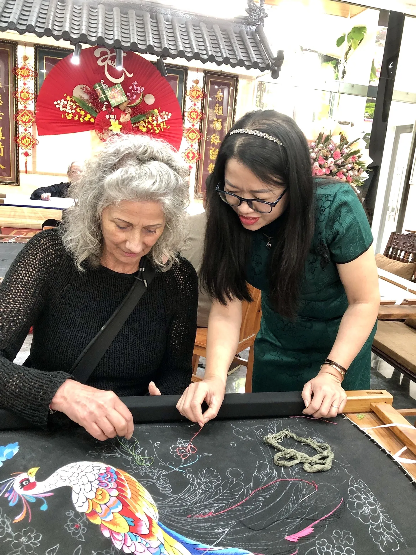 A local artisan helping a visitor learn traditional embroidery at Vị & Thêu