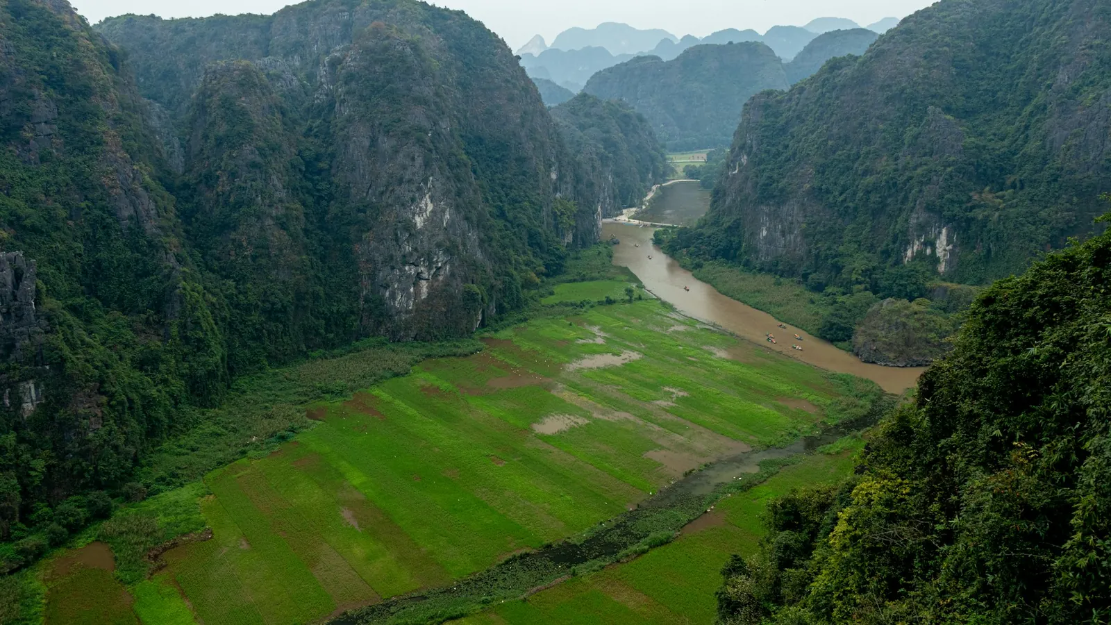 A river winding between green fields and limestone mountains in Tam Coc, Ninh Binh