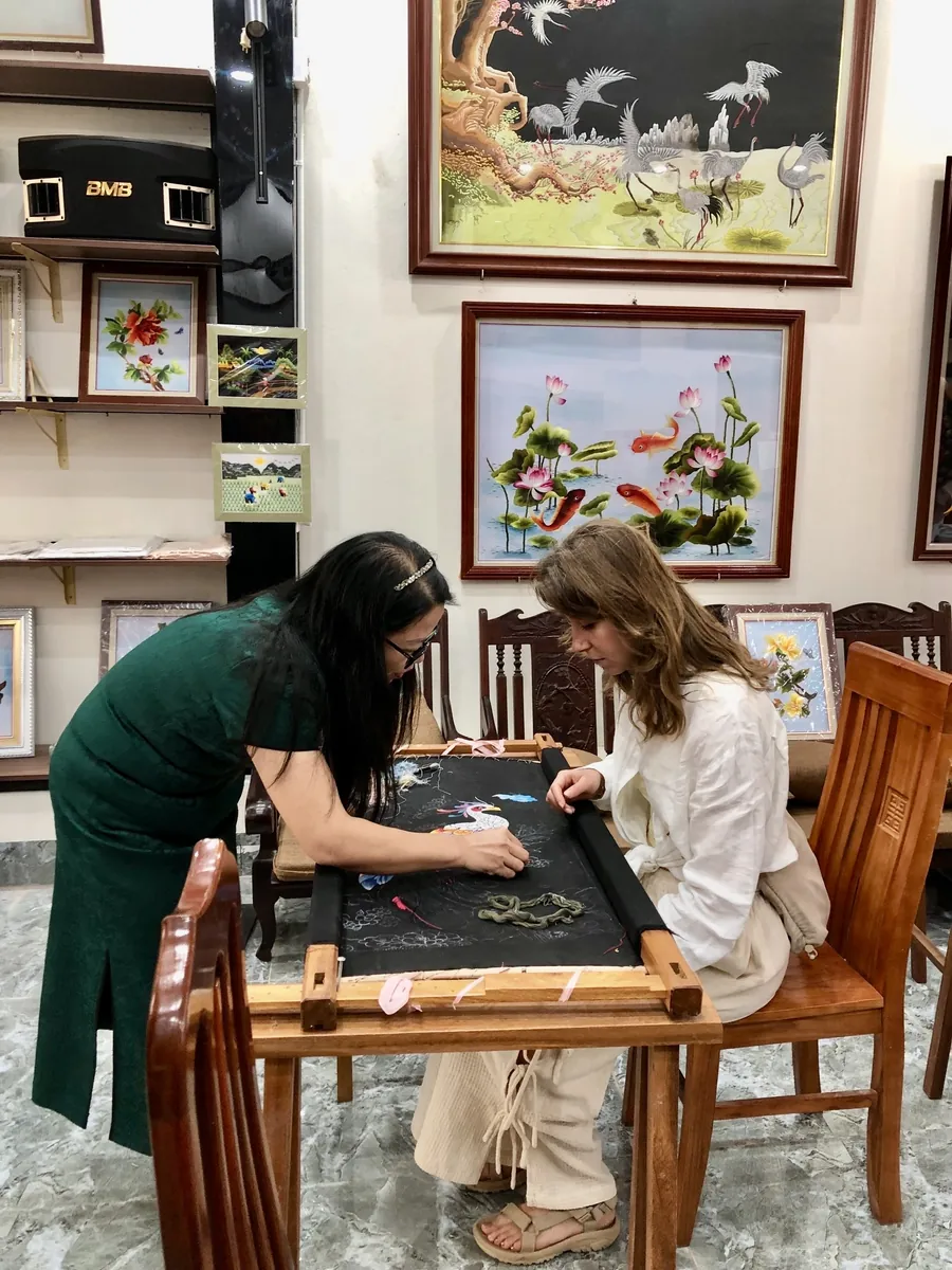 An artisan helping a participant with embroidery at Vị & Thêu