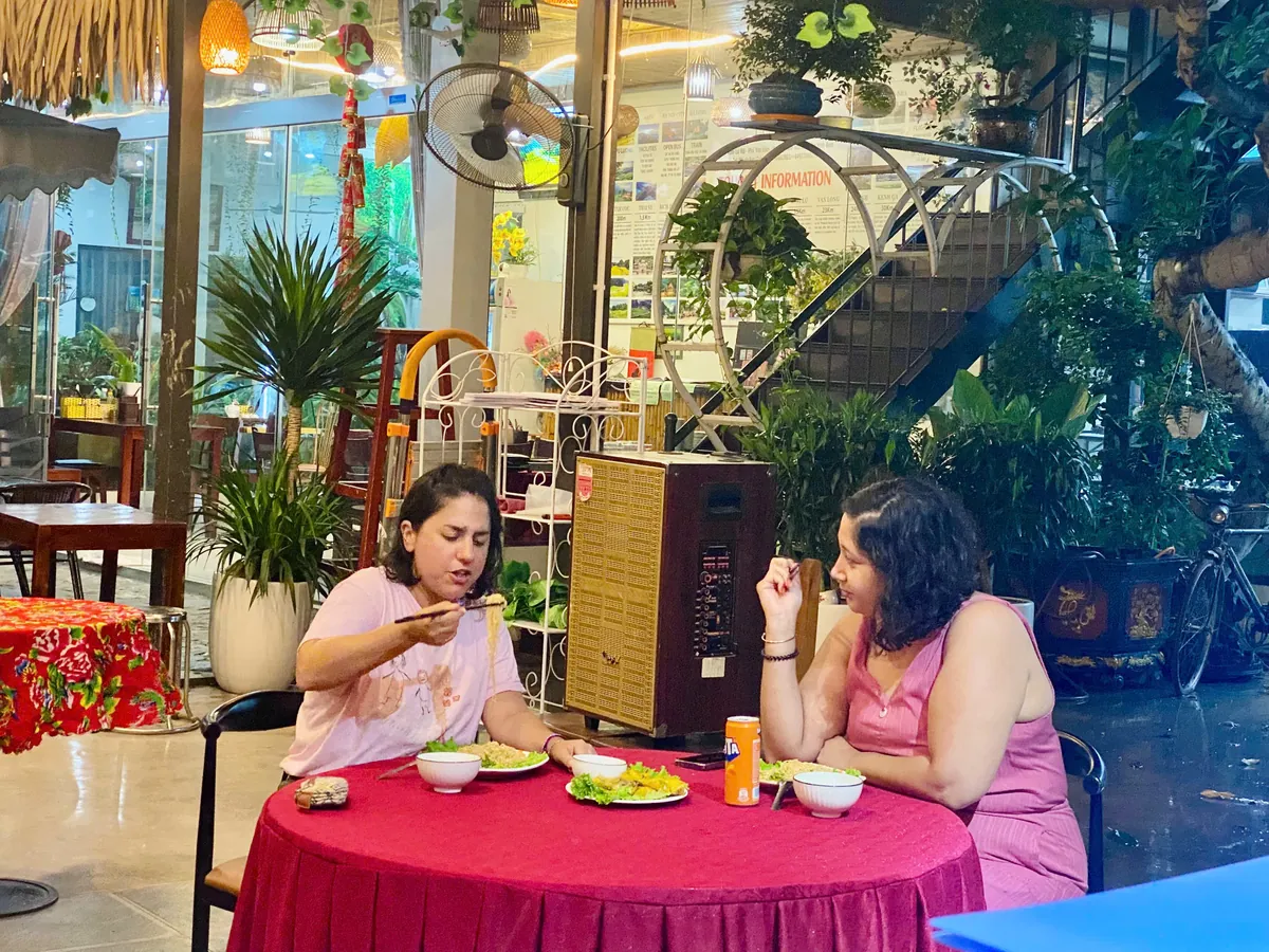 Two guests sharing a meal at a red-covered table at Vị & Thêu